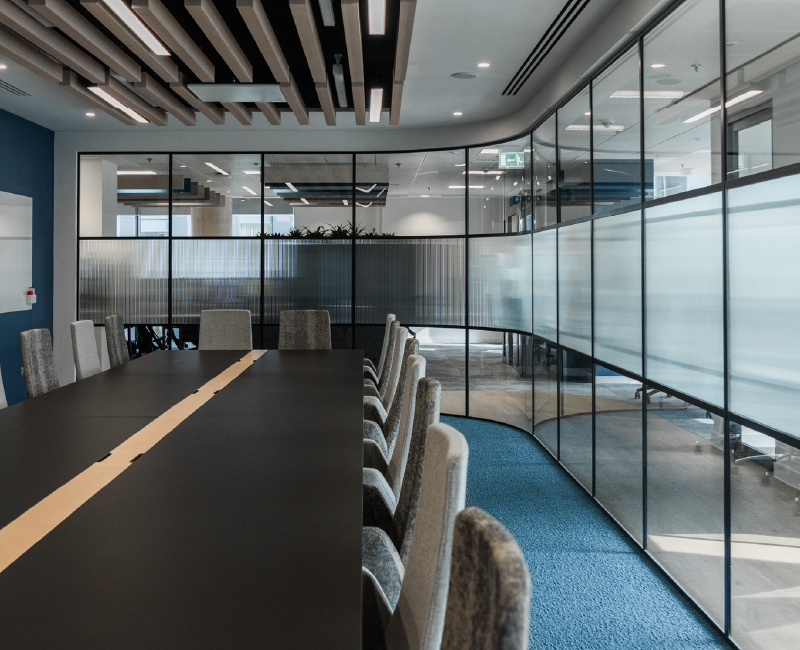 Board room complete with curved crittal glass, a large black table and wood effect acoustic ceiling rafts