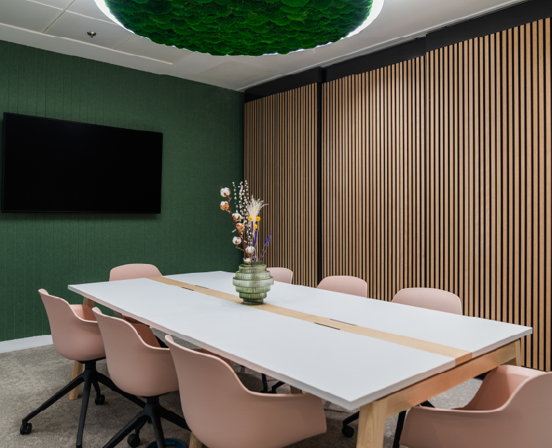 A meeting room with wooden acoustic wall panels, moss ceiling pendant light and eight person table